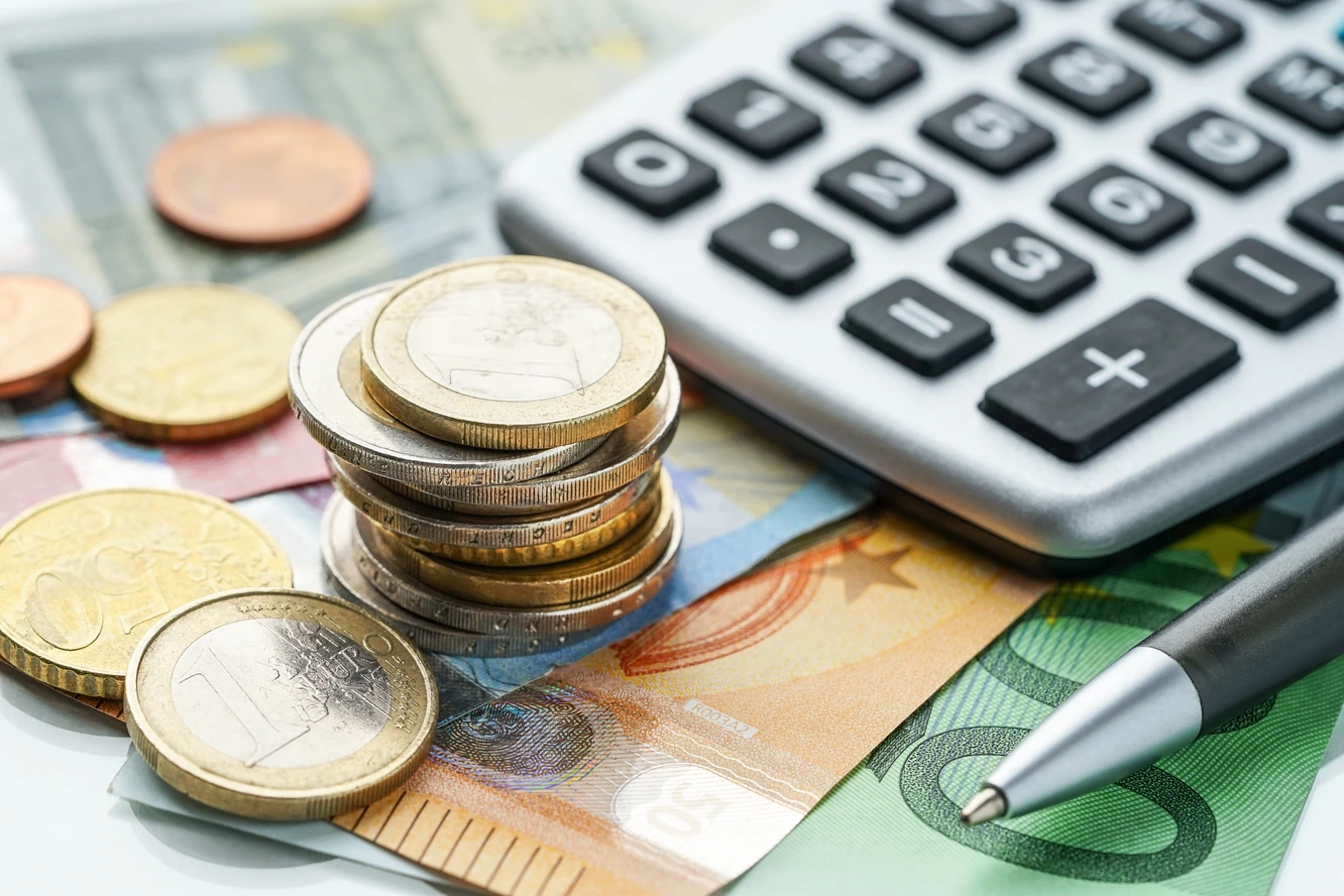 Euro-Banknoten und Münzen neben einem Taschenrechner und Stift. 